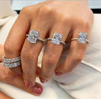 ladies hand wearing three radiant cut engagement rings and diamond eternity bands